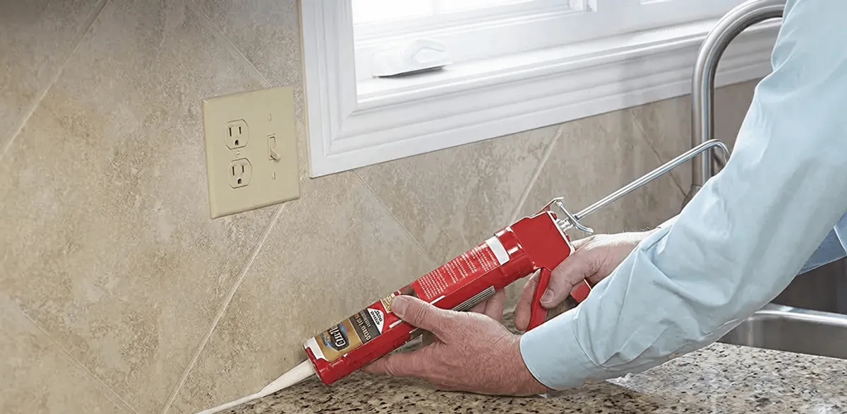 Handyman applying caulk along a kitchen backsplash and countertop seam in Colorado Springs, CO